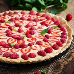 Tart with strawberries, raspberries and whipped cream decorated with mint leaves.
