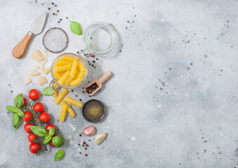 Penne pasta in glass jarl with parmesan cheese and tomatoes, basil with garlic and oil on light background.