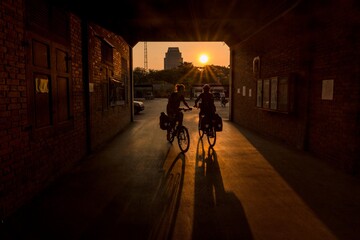 Fototapeta na wymiar Bangkok, Thailand: In the dark tone, silhouette cyclists is biking in the walkway tunnel early morning period which the sunlight is shining behind them through the entrance tunnel. 