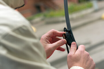 Man holds the latch on the wiper blade holder with his fingers on a blurry background