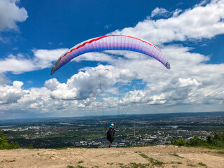 Paraglider taking off from the edge of the mountain over a city. Blue sky with clouds. Flying with a colordul parachute. Concept of freedom, relax, paragliding in the air