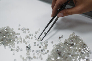 A hand holding tweezers transfers diamonds from one pile to another. Discarding precious stones on...