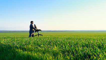businessman carries an office chair in a field to work, freelance and business concept, green grass and blue sky as background
