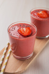 Close up a strawberry banana smoothie in glass on a wooden board on a white table. Food and healthy nutrition. Vertical orientation.