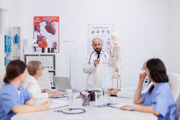 Obraz premium Physician doctor with stethoscope holding hand bone explaining body human skeleton presenting anatomy structure discussing medical expertise. Hospital team working in conference meeting room