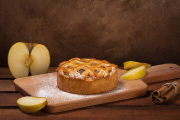 Fresh apples and apple pie on cutting wooden board with cinnamon roll On Brown Background