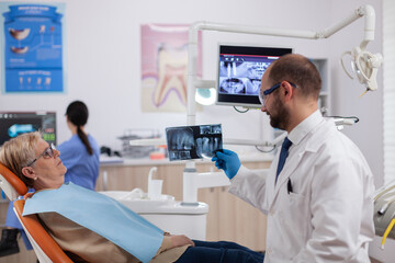 Dentist assistant giving doctor radiography of senior woman waiting. Medical teeth care taker...
