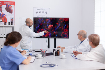 Obraz premium Virolog man specialist talking about coronavirus symptoms during virus presentation in front of practitioner doctors. Medical team of physicians planning vaccine against corona virus