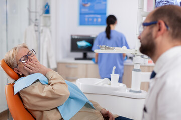 Elderly patient waiting diagnostic from dentist doctor sitting on dental clinic chair. Senior woman...