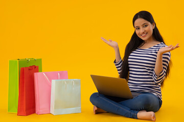 A young woman sitting with laptop and carrybags by her side.