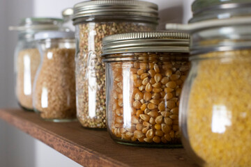 Close up of glass storage containers filled with grain and legumes on open pantry wooden shelf.