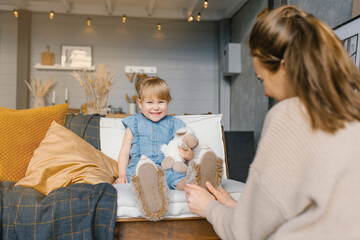 Mom puts on her daughter's slippers while sitting on the couch in the house