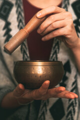 Fototapeta na wymiar hands of a woman using a golden tibetan bowl in a meditation dressed with a handmade poncho. background with copy space. concept meditation. vertical image
