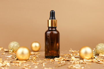 Obraz na płótnie Canvas Dropping essential oil in glass bottle, Christmas balls and pieces of gold paper firecracker on golden background, new Year party. Serum with hyaluronic acid in brown glass bottle. Mockup, front view.