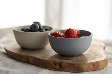Two bowls with fresh blueberries and strawberries on woo dboard