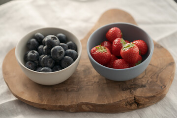 Two bowls with fresh blueberries and strawberries on woo dboard