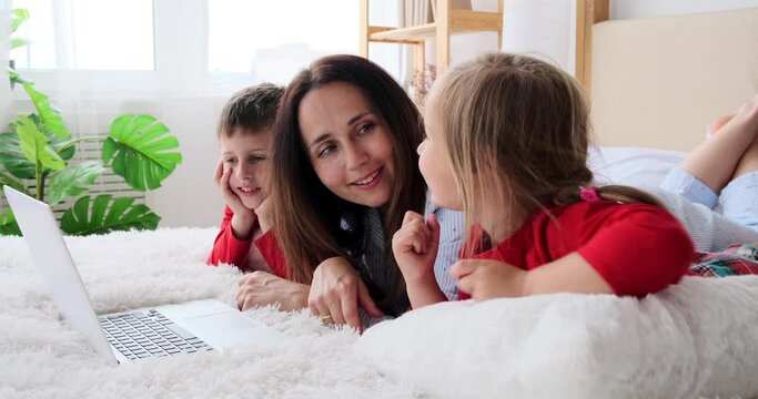 Mother with children watching movie using laptop on bed at home