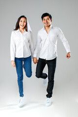 Young attractive Asian couple wearing white shirt and veil holding hands jumping and smiling against white background. Concept for pre wedding photography. Isolate