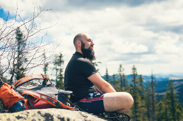 Hiker with backpack sitting on rocks in the mountain and looking into the distance.