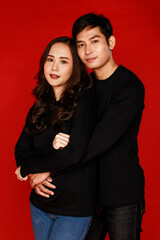 Young attractive Asian couple wearing black shirt and jeans holding each other against red background. Concept for pre wedding photography. Isolated