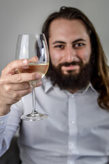portrait of a young middle eastern businessman with beard and long hair holding a glass of fresh white wine, focus on the wineglass