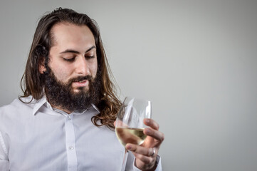 portrait of a young middle eastern businessman with beard and long hair holding a glass of fresh white wine and looking at its color