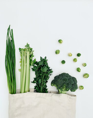 Top view of green vegetables in an eco cotton tote bag on a white background.