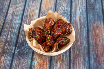BBQ wings with lots of sauce drizzled with sesame seeds, chopped chives and cardboard bowl for home delivery