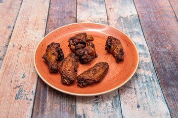 Ration of fried wings butt with barbecue sauce on red plate with wooden table in a cheap restaurant