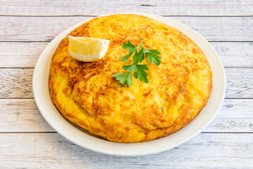 Spanish potato omelette with parsley on top and lemon to garnish served in a tapas restaurant