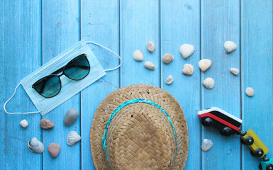 Summer flat lay on the theme of recreation and travel. Protective medical mask, sunglasses, toy train, pebbles and shells on a blue wooden background. Features of rest during the coronavirus pandemic