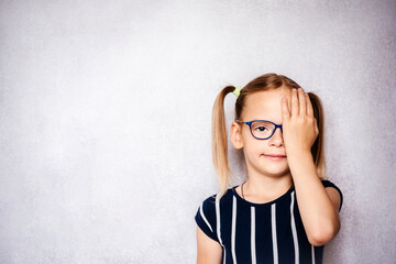 Little girl in eyeglasses covering her eye with her hand while taking eyesight test before school,...