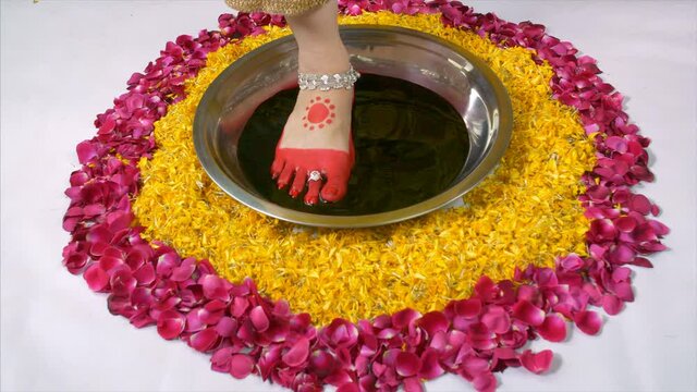 Closeup shot a beautiful Indian bride's performing Griha Pravesha rituals. High angle shot - Legs of a newly married woman stepping into a dish of Alta during Griha Pravesha ceremony