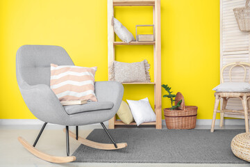 Trendy interior of living room with grey armchair and yellow wall