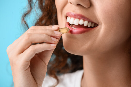 Young Woman Taking Fish Oil Pill On Color Background