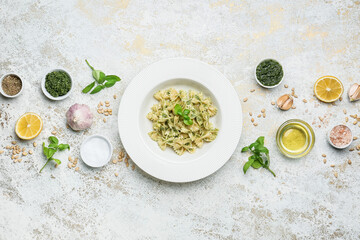 Plate with tasty pesto pasta and ingredients on light background