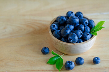 Closed up fresh blueberry fruit with green leaf in wooden bowl