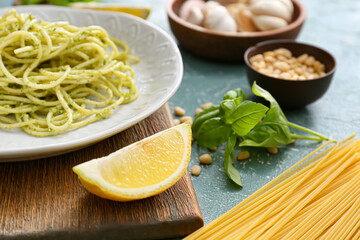 Piece of lemon and plate with tasty pesto pasta on table