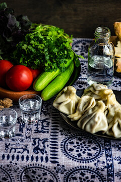 Fresh khinkali dumplings, tomatoes, cucumber, spring onion, coriander and basil on a plate on a table with glasses of chacha