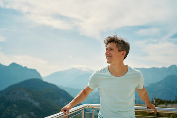 Positive happy man tourist enjoying fresh air at viewpoint among mountains and cloudy sky. travel...