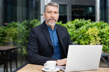 Handsome middle age man using laptop computer in a city. Mature man working outdoors. Modern...