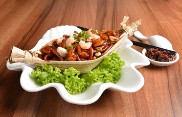 stir fried hokkien dark soy sauce udon noodle with seafood and meat in leaf on wood table asian...