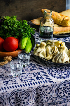 Fresh khinkali dumplings, tomatoes, cucumber, spring onion, coriander and basil on a plate on a table with glasses of chacha