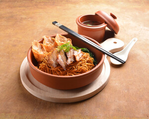 cook dry wanton yellow noodle with deep fried dumpling, char siew meat and soup bowl on wood table...