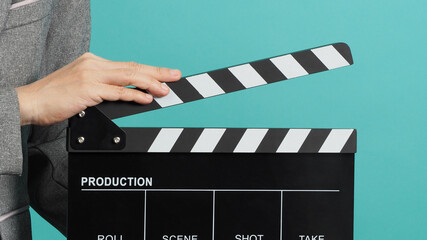 Black Clapperboard or movie Clapper board for videography with hands in grey suit . it use in video production ,movies and cinema industry on green Tiffany Blue background.director film slate