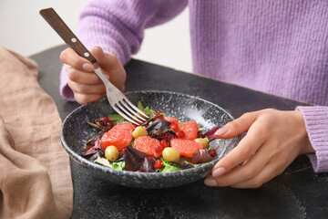 Woman eating tasty grapefruit salad at dark table, closeup