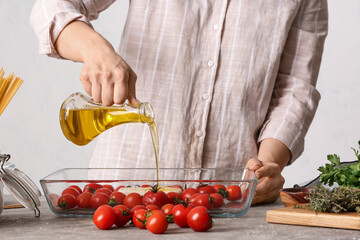 Woman preparing tomatoes and feta cheese for baking in kitchen