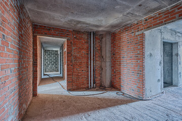 Apartment interior without finishing. Room in new building without repair, red brick walls are not plastered. Repair works on construction site of residential apartment.