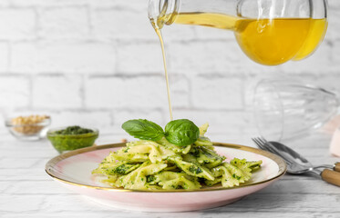 Pouring of olive oil from bottle onto plate with tasty pesto pasta on table