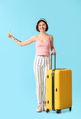 Young woman with suitcase hitchhiking on color background